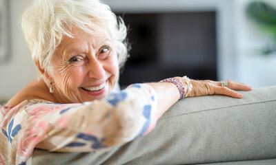 foto van een senior dame die over de leuning van een sofa kijkt