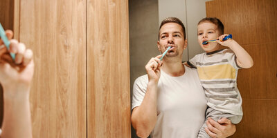 Man en kind die samen hun tanden aan het poetsen zijn 